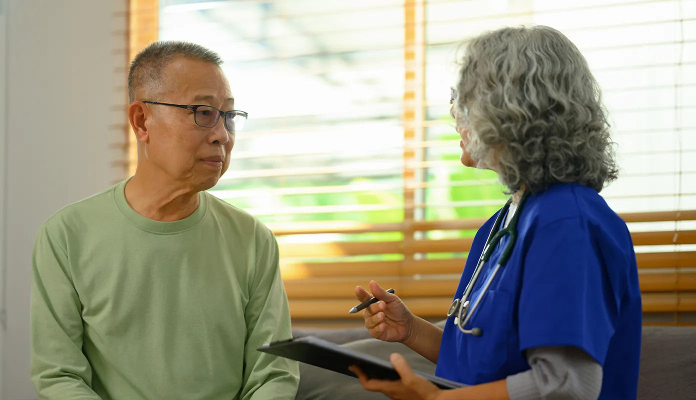 Clinician with clipboard talking to asian man.