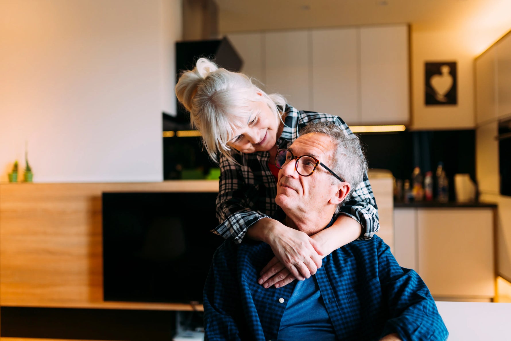 Old couple smiling and hugging while looking at each other in a home setting.
