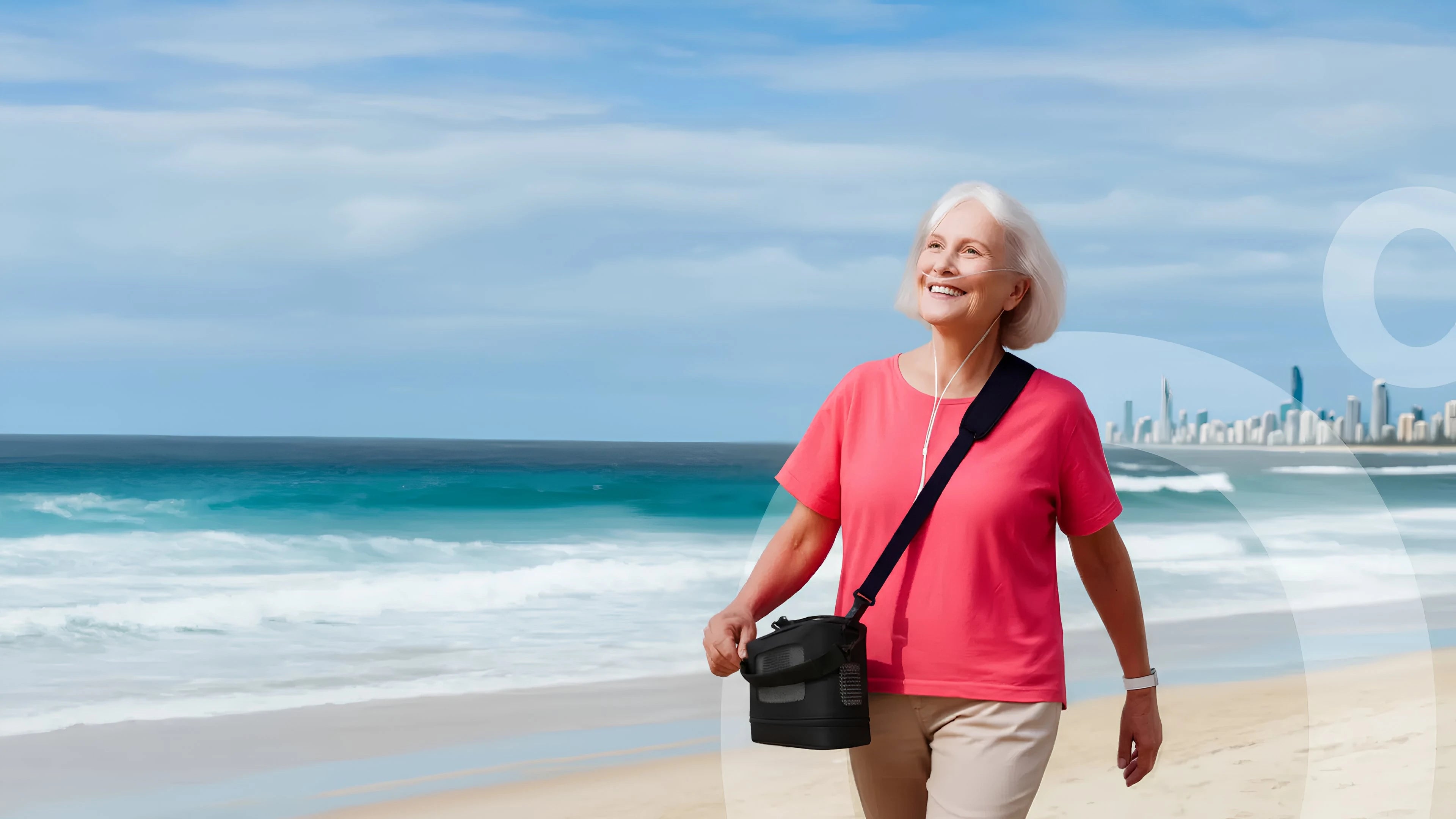 Woman smiling and walking on a beach while using a Kingon P2 portable oxygen concentrator. Clear blue sky and ocean in the background.