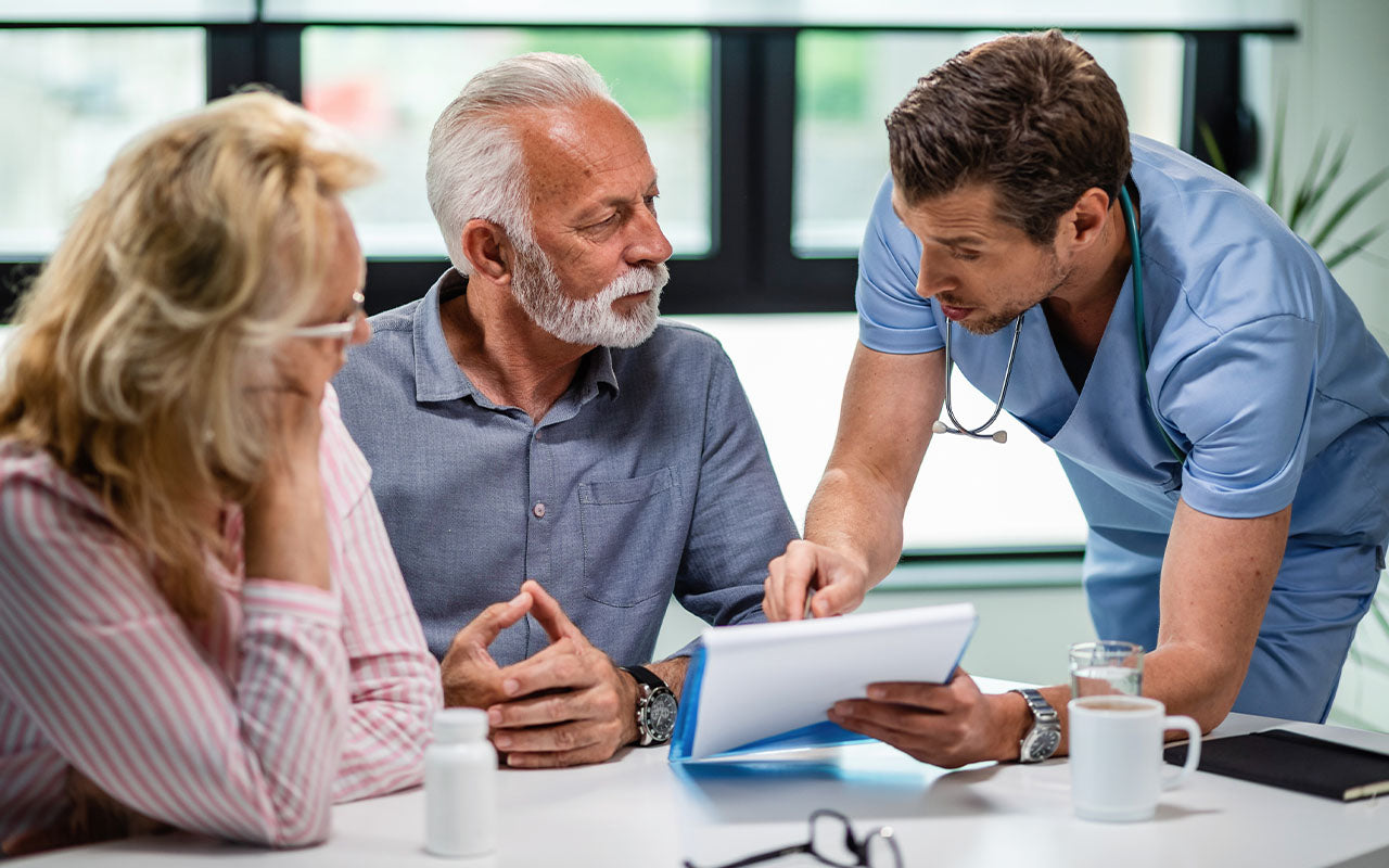 A practitioner explaining with a clip board to an old couple.