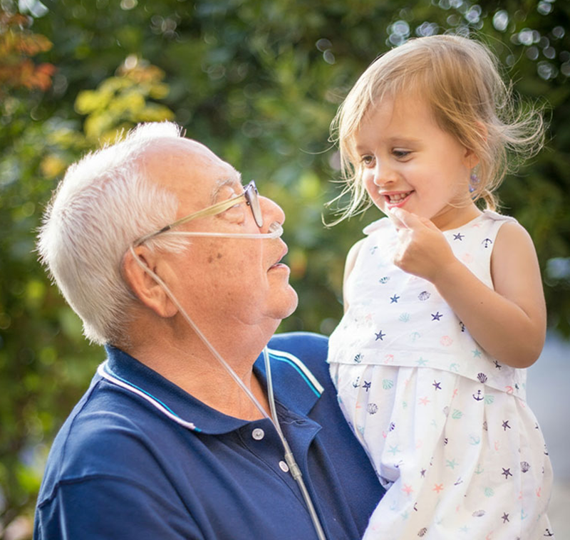 Old man with a nasal cannula on carrying his grandchild outside.