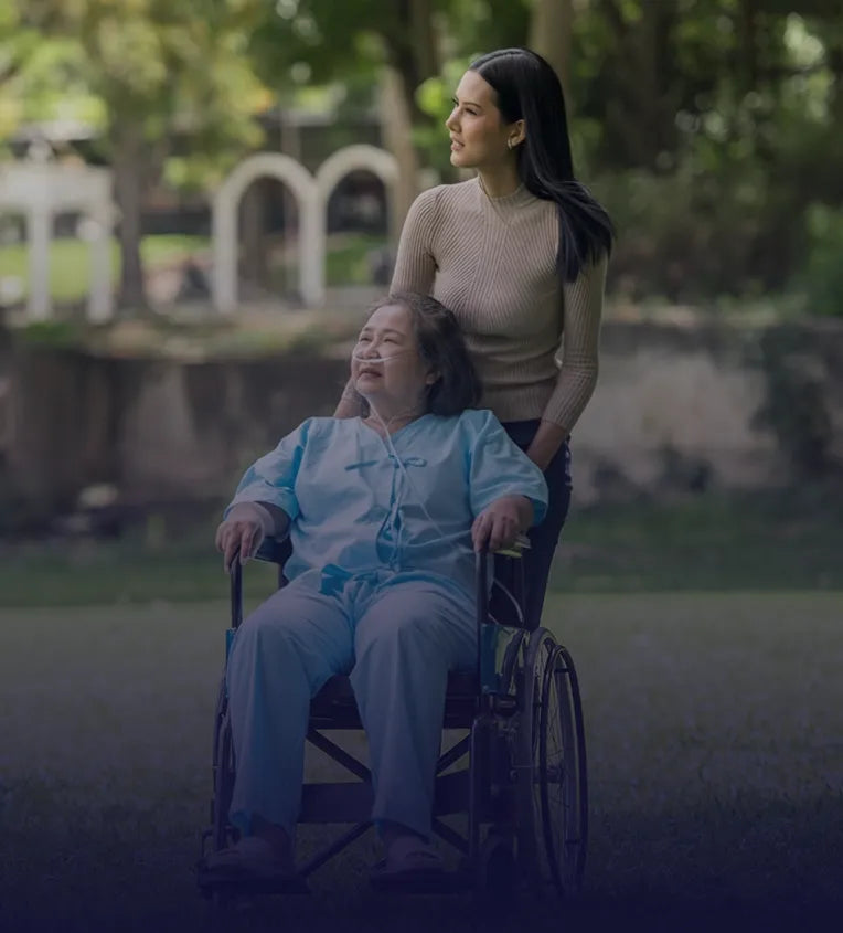 Carer pushing old woman in a wheelchair through a park.