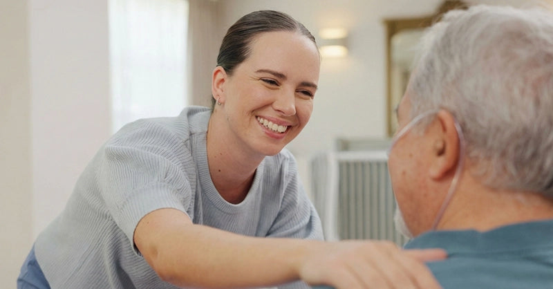 Aged care worker smiling with hand on patient shoulder.